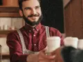 Barista souriant, chemise à motif CDD, sert un café.