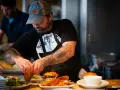 Un chef tatoué prépare des burgers et des frites, gage d'assurance restauration rapide.