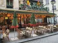 Terrasse de café parisien, tables et chaises en rotin, parasols verts. La réglementation terrasse sur trottoir est respectée.
