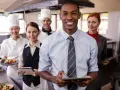 Une équipe souriante en cuisine, le responsable vérifie l'horaire collectif de travail sur sa tablette.