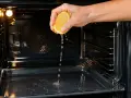 Une main presse un citron pour degraisser un four tres sale. Le jus coule sur la plaque.
