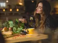 Une femme savoure un plat de pâtes dans un restaurant. Son expression suggère un avis très positif sur le repas.