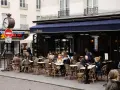 Terrasse animée d'un restaurant parisien, le Café Delmas, où des clients profitent de l'extérieur. Pas de tapage nocturne ici, juste une ambiance de bistrot paisible.