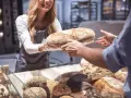 Une boulangère souriante offre une miche de pain frais, célébrant la journée mondiale de la pâtisserie.