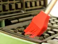 Un pinceau rouge nettoie les recoins d'un gaufrier encrassé.