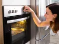 Une femme ajuste le bouton du four pour savoir à quelle température faire réchauffer un plat. Le plat est visible à travers la vitre.