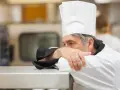 Un chef fatigué, le visage caché dans son bras, semble épuisé par un long jour de carence restauration rapide.