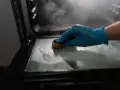 Main gantée bleue pour nettoyer le four avec du bicarbonate. La vapeur s'échappe, signe que le bicarbonate a chauffé.