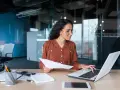 Femme travaillant sur un ordinateur portable, tenant des documents. Elle semble réfléchir à une décision unilatérale de l'employeur.