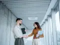 Un homme et une femme se serrent la main dans un couloir moderne, signe d'une prime cooptation réussie.