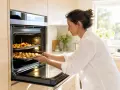 Une femme met des plats dans un four. Elle découvre la différence entre chaleur tournante et convection en cuisinant.