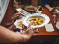 Un serveur présente une assiette de tortellinis dans un bouillon. Le service en restauration est à son apogée.