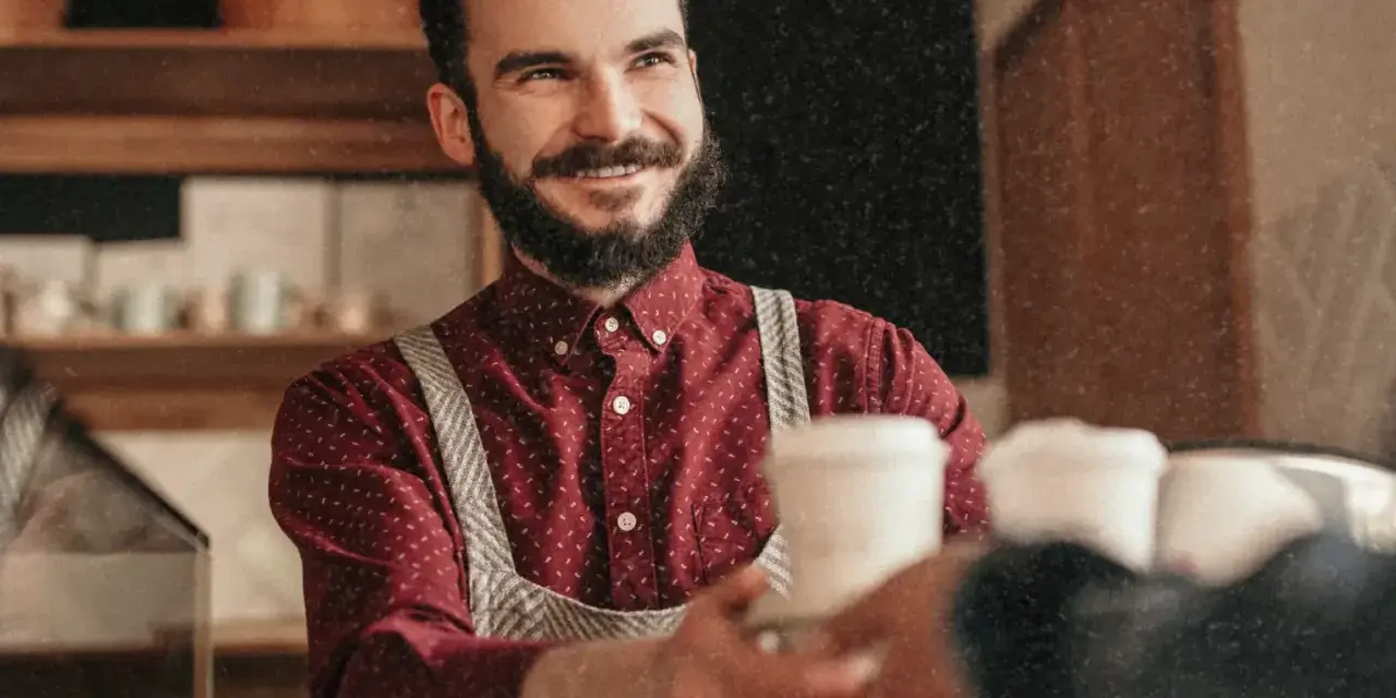 Barista souriant, chemise à motif CDD, sert un café.