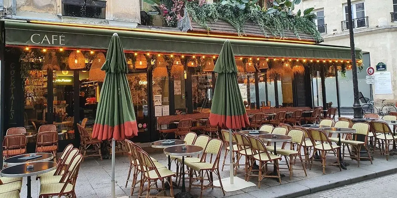Terrasse de café parisien, tables et chaises en rotin, parasols verts. La réglementation terrasse sur trottoir est respectée.