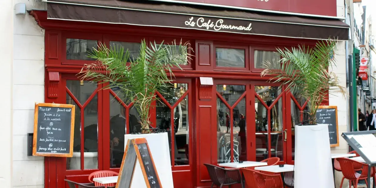 Le Café Gourmand, un restaurant aux noms originaux, invite à la dégustation avec sa façade rouge vif et ses palmiers.