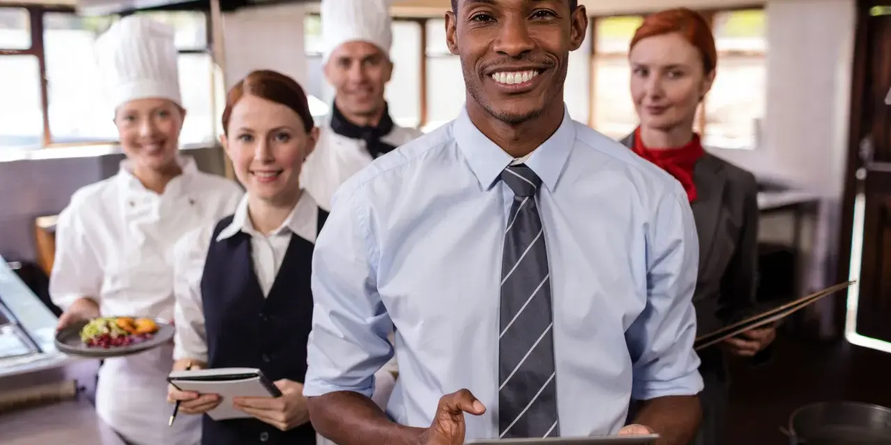 Une équipe souriante en cuisine, le responsable vérifie l'horaire collectif de travail sur sa tablette.