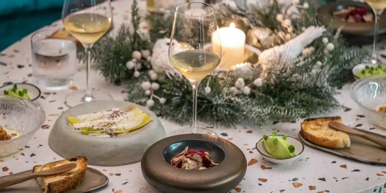 Une table dressée pour une fete gastronomique, avec des verres de vin, des amuse-bouches et une décoration hivernale.