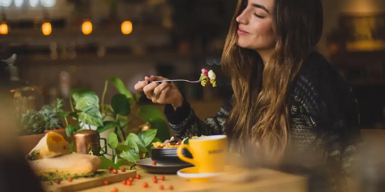Une femme savoure un plat de pâtes dans un restaurant. Son expression suggère un avis très positif sur le repas.