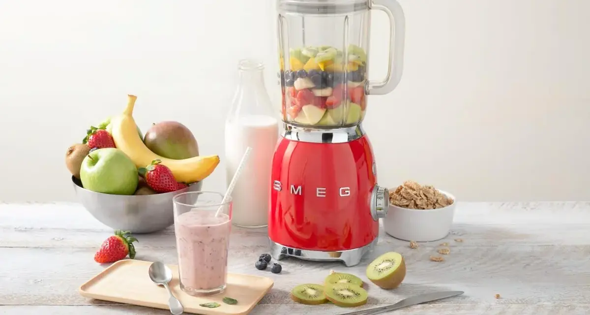 Un blender rouge SMEG, rempli de fruits, prêt à préparer un smoothie. Il montre à quoi sert un blender : mixer des ingrédients pour des boissons saines et délicieuses.