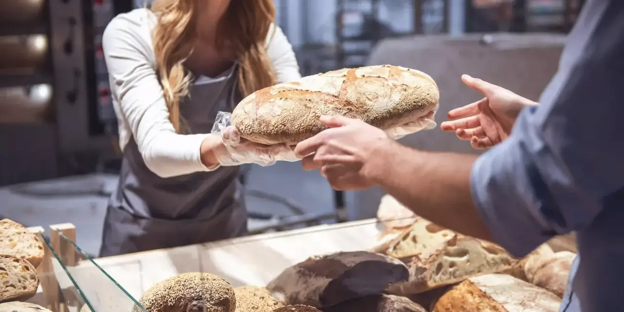 Une boulangère souriante offre une miche de pain frais, célébrant la journée mondiale de la pâtisserie.