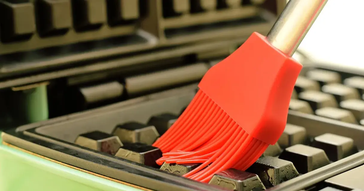 Un pinceau rouge nettoie les recoins d'un gaufrier encrassé.