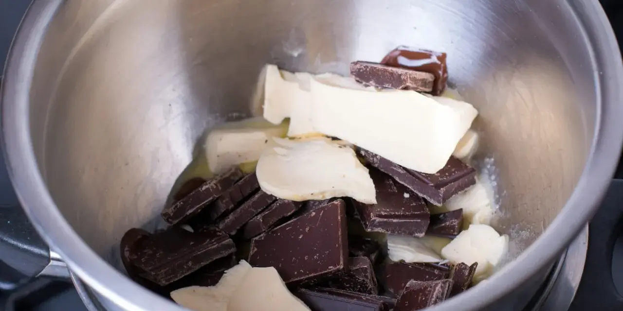Morceaux de chocolat noir et de beurre dans un bol en métal, prêts pour une cuisson au bain-marie au four.