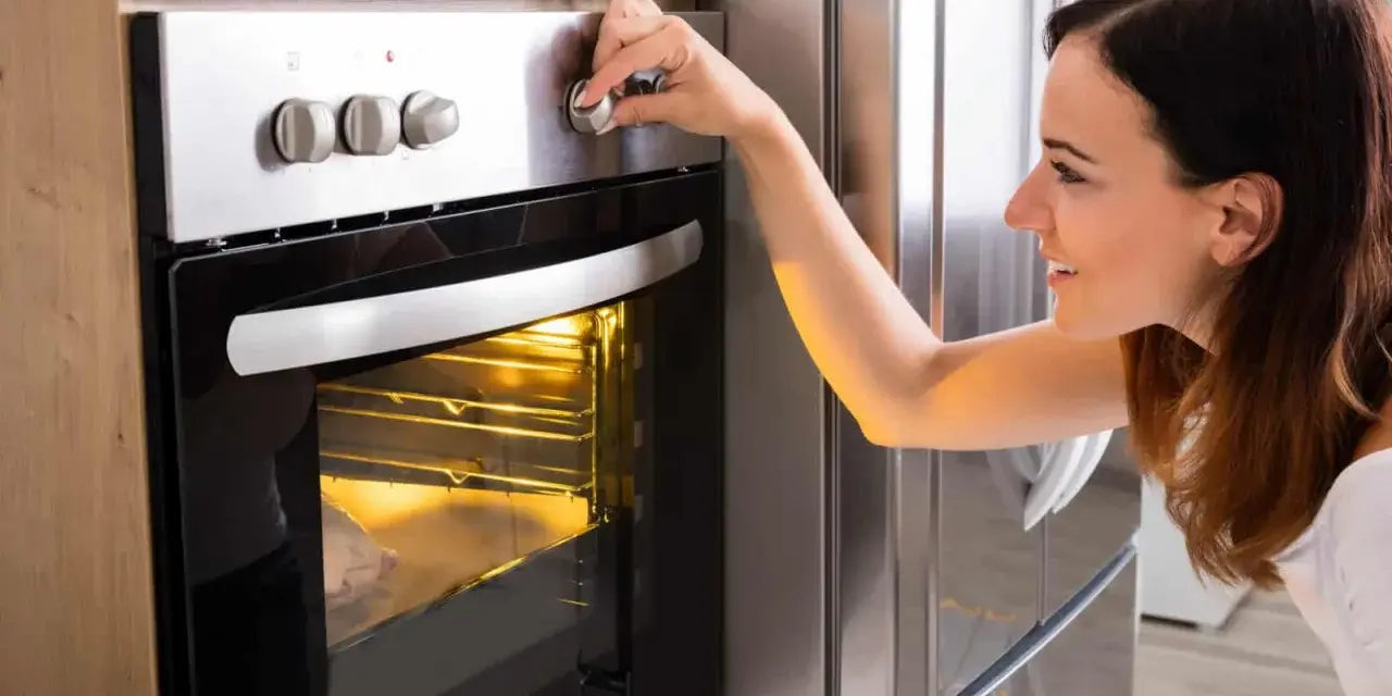 Une femme ajuste le bouton du four pour savoir à quelle température faire réchauffer un plat. Le plat est visible à travers la vitre.