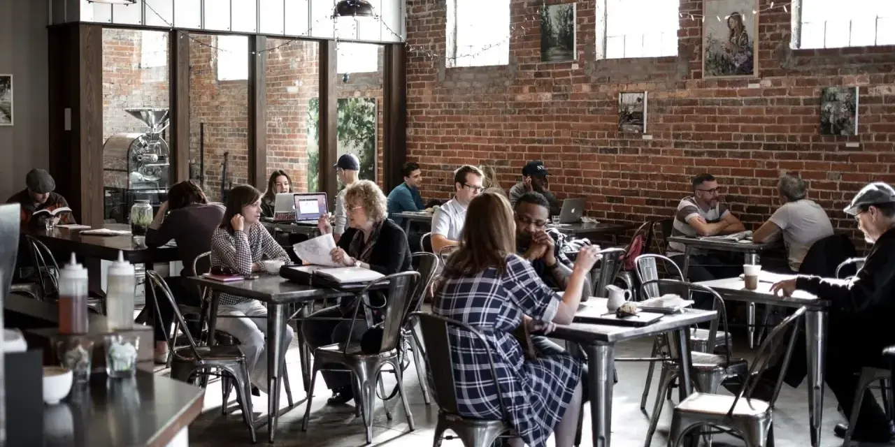 Ambiance de café animée, des gens travaillent et discutent. Un dimanche payé double pour la restauration, l'atmosphère est détendue.