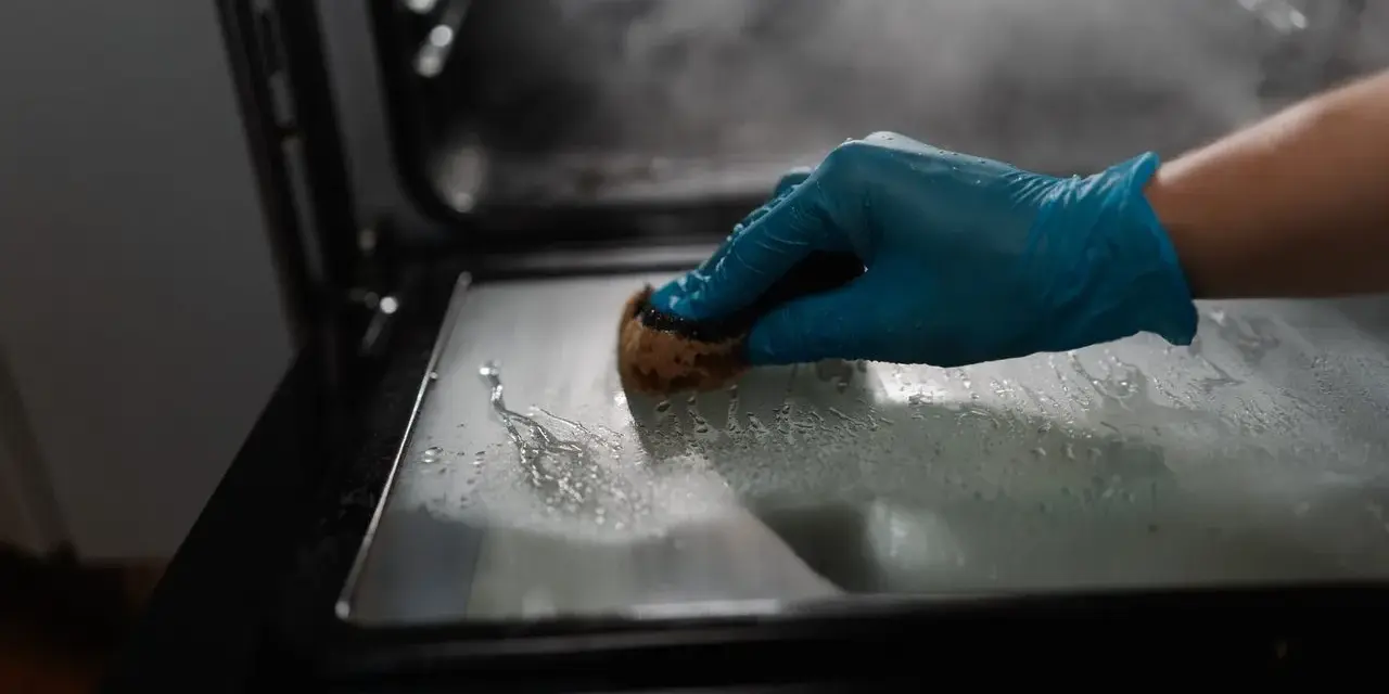 Main gantée bleue pour nettoyer le four avec du bicarbonate. La vapeur s'échappe, signe que le bicarbonate a chauffé.