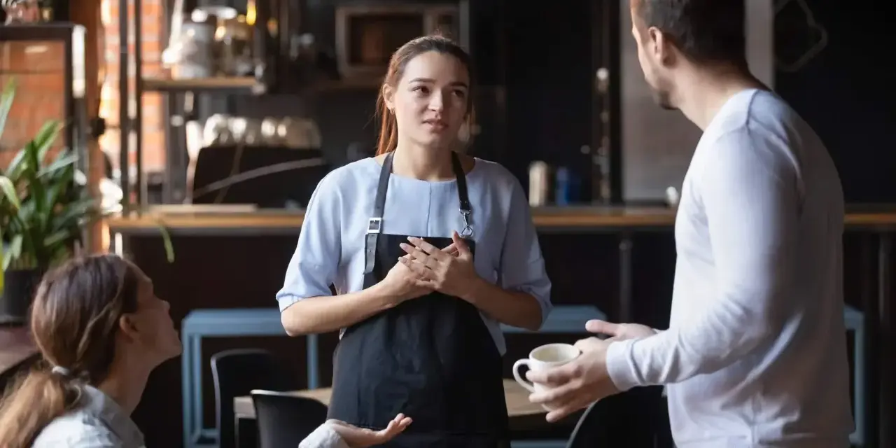 Serveuse attentive face à une cliente mécontente exprimant sa frustration. La serveuse écoute avec empathie.