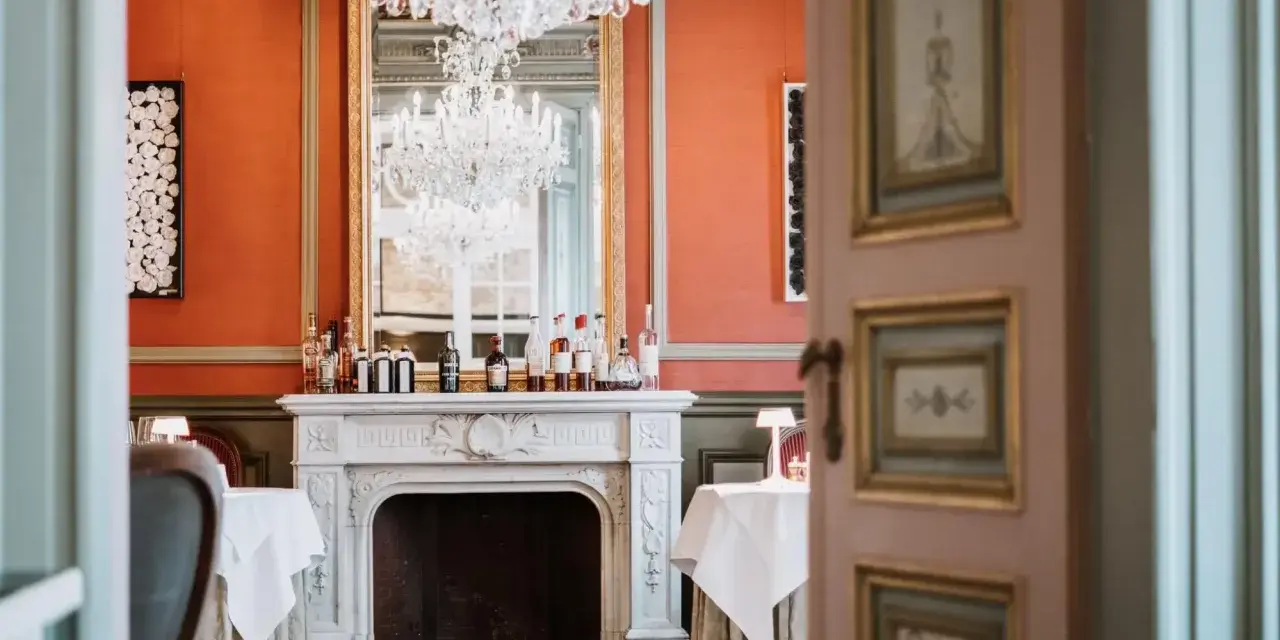Salle à manger élégante avec cheminée, lustres et tables dressées. Un décor parfait pour savoir comment être référencé dans le Petit Futé.