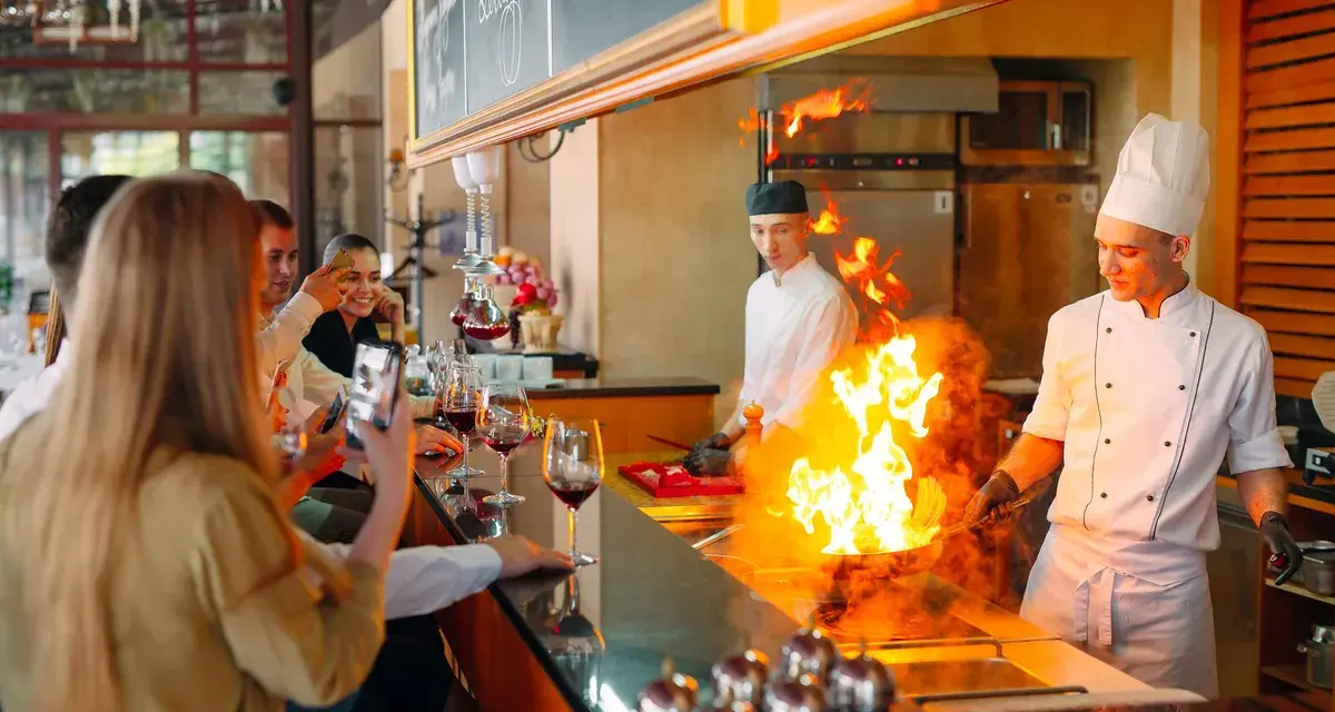 Cuisine ouverte d'un restaurant, chefs en action avec des flammes impressionnantes. Des clients prennent des photos, respectant la norme.