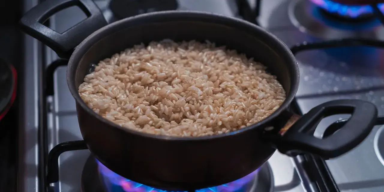 Un pot de riz brun est chauffé doucement sur une cuisinière à gaz, les flammes bleues dansant sous le récipient, pour réchauffer du riz au bain-marie.
