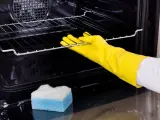 Main tenant porte-gants jaunes pour nettoyer le four. Une éponge bleue et blanche est posée sur le fond du four.