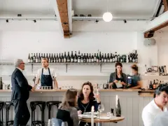 Un bar de restaurant animé avec un personnel attentif, des bouteilles de vin alignées et des clients profitant de l'ambiance. La gestion du restaurant assure un service fluide.