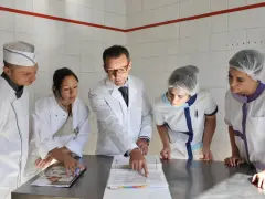 Cinq personnes en tenue de cuisine étudient des documents. Le chef montre un point précis, peut-être pour un double emploi ou une nouvelle procédure.