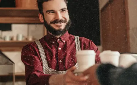 Barista souriant, chemise à motif CDD, sert un café.