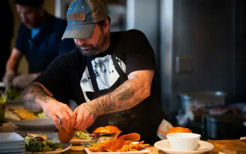 Un chef tatoué prépare des burgers et des frites, gage d'assurance restauration rapide.