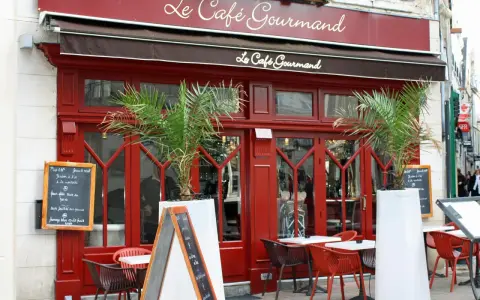 Le Café Gourmand, un restaurant aux noms originaux, invite à la dégustation avec sa façade rouge vif et ses palmiers.