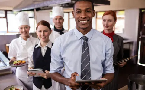 Une équipe souriante en cuisine, le responsable vérifie l'horaire collectif de travail sur sa tablette.