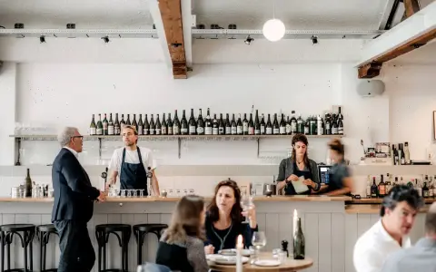 Un bar de restaurant animé avec un personnel attentif, des bouteilles de vin alignées et des clients profitant de l'ambiance. La gestion du restaurant assure un service fluide.