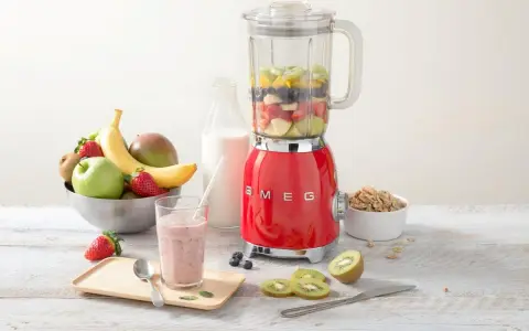 Un blender rouge SMEG, rempli de fruits, prêt à préparer un smoothie. Il montre à quoi sert un blender : mixer des ingrédients pour des boissons saines et délicieuses.