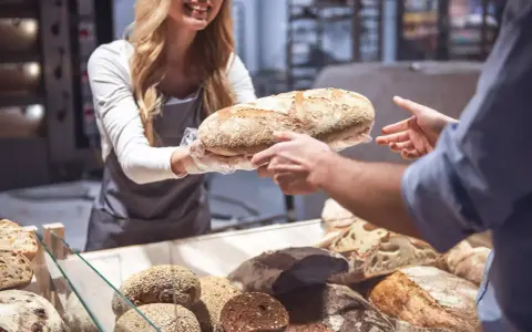 Une boulangère souriante offre une miche de pain frais, célébrant la journée mondiale de la pâtisserie.