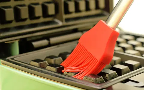 Un pinceau rouge nettoie les recoins d'un gaufrier encrassé.