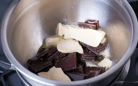 Morceaux de chocolat noir et de beurre dans un bol en métal, prêts pour une cuisson au bain-marie au four.