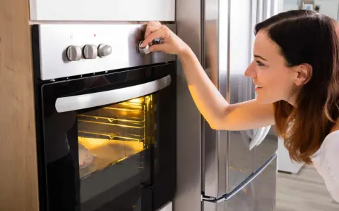 Une femme ajuste le bouton du four pour savoir à quelle température faire réchauffer un plat. Le plat est visible à travers la vitre.