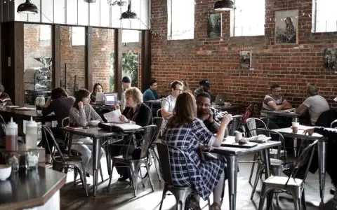 Ambiance de café animée, des gens travaillent et discutent. Un dimanche payé double pour la restauration, l'atmosphère est détendue.