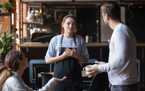 Serveuse attentive face à une cliente mécontente exprimant sa frustration. La serveuse écoute avec empathie.