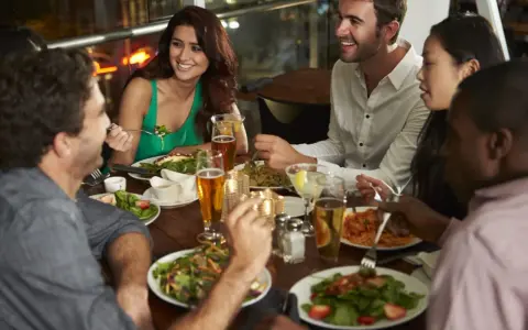 Un groupe d'amis partage un repas animé dans un restaurant, une excellente idée soirée à thème restaurant. Ils rient et discutent autour d'une table garnie de plats et de boissons.
