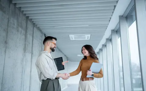 Un homme et une femme se serrent la main dans un couloir moderne, signe d'une prime cooptation réussie.